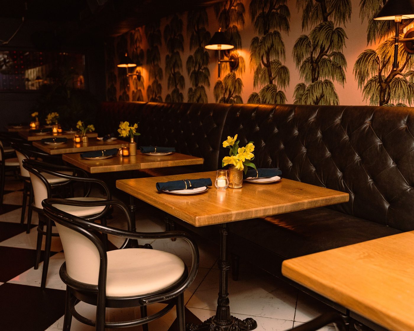 Candlelit tables along the tufted leather banquette, beneath willow wallpaper