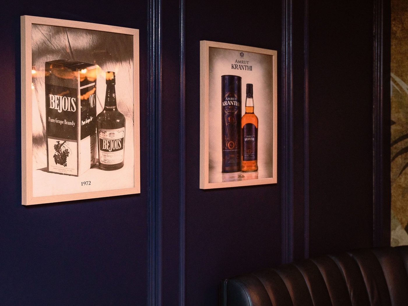 Framed Amrut bottles from 1972 and 2026 on the dark panelled wall